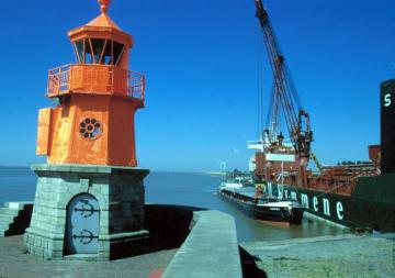 Blick auf den Hafenleuchtturm und einen Überseefrachter während der Verladung von Zellulose auf den Binnenfrachter Libertas
