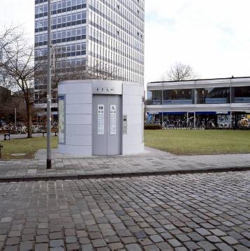 Modernes Toilettenhaus am Servatiiplatz, im Hintergrund das IDUNA-Hochhaus (Baudenkmal) und Fahrradgeschäft "Drahtesel"