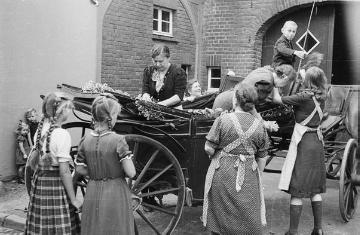Nachbarn schmücken eine Kutsche für die Abreise von Auswanderern der Familie Fels nach Amerika. Nottuln, Burgstraße, Ende 1940er Jahre.