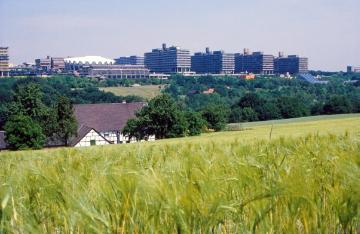 Die Ruhr-Universität Bochum - Campus-Universität im Bochumer Süden: Hälftige Teilansicht des Universitätsgeländes mit dem Auditorium Maximum (weißes Dach) und den (N-)Gebäuden der naturwissenschaftlichen Fakultäten - hinter dem Kornfeld der Botanische Garten