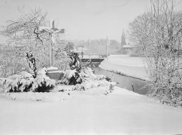 Harsewinkel: winterliche Ortsansicht am Abroocksbach mit Wegekreuz Münsterstraße, Nähe Brückenweg, St. Lucia-Kirche in der Ferne. Undatiert, um 1960?