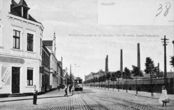 Hamm - Wilhelmstraße mit Straßenbahnverkehr (Trassenbau ab 1898) und junger Baumreihe. Rechts: Werkshallen der WDI (Westfälische Drahtindustrie). Im Vordergrund: "Bürgerliches Logierhaus" (Gaststätte Fritz Sippel), Wihelmstraße 28. Postkarte, undatiert, um 1910.