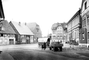 Delbrück-Ortszentrum um 1951: Lange Straße (vorn) und Alter Markt, bis 1937 Wochenmarktplatz. V.l.n.r.: Gasthaus "Ottlips Lieschen" (Lange Straße 2), Haus Melcher und Haus Schnittker, Postamt (später Filiale der Volksbank OWL), Häuser Brenken und Menneken.