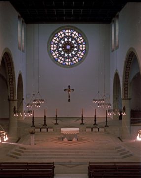 Blick in eine Kirche: Altarraum mit Rosettenfenster, Mikrophonpult (Steinsockel mit Bronzeaufsatz - vorn links), Steinaltar mit bronzenem Kruzifix und Bronzeleuchtern. Unbezeichnet, undatiert.
