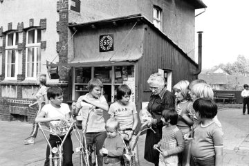 "Oma Olschewski" mit Kindertrupp, August 1976: Emmy Olschewski (1904-1998) vor ihrer 1921 erröffneten Trinkhalle an der Schweriner Straße in Castrop-Rauxel-Schwerin. [Nach ihrem Tode 1998 wurde die Trinkhalle in das Inventar eines Industriemuseums des Landschaftsverbandes Westfalen-Lippe überführt.]