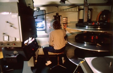 Unbekanntes Kino. Technikraum. Eine Person bedient den Filmprojektor (links), Telleranlage (rechts).
