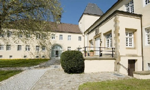 Auf dem Bild ist das cremefarbene Schlossgebäude mit seinem Torbogen zu sehen. In dem Raum hinter dem Torbogen ist ein Besprechungssaal. Auf dem Bild ist das cremefarbene Schlossgebäude mit seinem Torbogen zu sehen. In dem Raum hinter dem Torbogen ist ein Besprechungssaal.