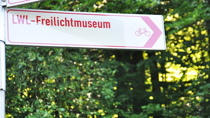 Ein Schild vom Radverkehrsnetz, das den Weg zum Museum weist. Auf dem Schild ist die Aufschrift LWL-Freilichtmuseum mit einem Fahrradsymbol.