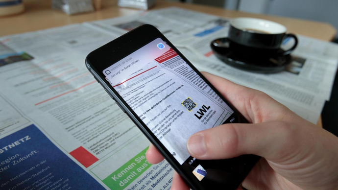 Eine Interessentin liest eine Stellenanzeige der LWL.IT in der Zeitung und scannt mit ihre Smartphone den QR-Code für weitere Informationen zum LWL Eine Interessentin liest eine Stellenanzeige der LWL.IT in der Zeitung und scannt mit ihre Smartphone den QR-Code für weitere Informationen zum LWL