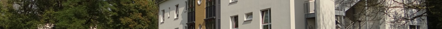 Sonnenbeschienene Gartenansicht der Fassade des Wolfgang-Leonhardt-Hauses auf dem LWL-Klinikgelände. Im Vordergrund hölzerne Sitzgelegenheiten