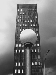 Das schwarz-weiß Foto zeigt eine kugelförmige Straßenlampe vor einem Hochhaus. Die Bildanordnung ist zentriert und symmetrisch.