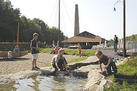 Das Bild zeigt einen Wasserlauf, den Kinder gerade gestaut haben. Im Hintergrund ist das Museumsgel�nde mit Ringofen zu sehen.