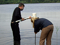 Zwei Personen entnehmen eine Grundwasserprobe am Seeufer