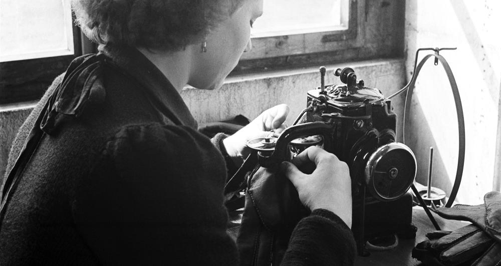 Schwarz-weiß Fotografie einer Näherin bei der Arbeit an der Nähmaschine. (vergrößerte Bildansicht wird geöffnet)