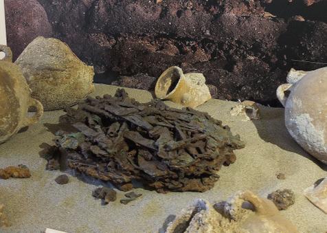 Im Archäologie-Museum Populonia liegt ein Haufen Klingen vor einem Bodenprofil aus Baratti, darum verteilt Bruchstücke von Amphoren. (vergrößerte Bildansicht wird geöffnet)