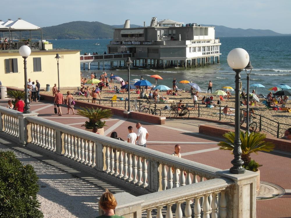 Im Vordergrund ist eine Strandpromenade zu erkennen, an die ein schmaler, mit Sonnenschirmen übersähter Strand anschließt und im Hintergrund ragt die Landungsbrücke mit einem Restaurant ins Meer. (vergrößerte Bildansicht wird geöffnet)