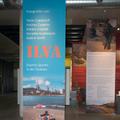 Von der Decke hängt das Banner der Ausstellung, während im Hintergrund weitere Banner mit Informationstexten und Illustrationen zu sehen sind. (vergrößerte Bildansicht wird geöffnet)