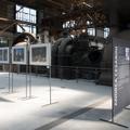 Vor einer stillgelegten Industriemaschine sind stehen drei Fotografien des Fotografen Andrea Cesarini. (vergrößerte Bildansicht wird geöffnet)