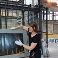 Eine junge Frau hält vorsichtig mit weißen Baumwollhandschuhen ein gerahmtes Foto der Ausstellung. (vergrößerte Bildansicht wird geöffnet)
