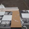 Zwei großflächige, quadratische Bilder, auf denen jeweils fünf quadratische Fotos angeordnet sind, liegen zusammen mit Verpackungsmaterial auf dem Boden. (vergrößerte Bildansicht wird geöffnet)