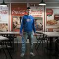 Ein junger Mann steht zwischen Tischen und Stühlen eines Restaurants. (vergrößerte Bildansicht wird geöffnet)