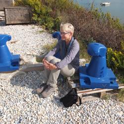 Eine Frau sitzt mit dem Rücken zum Meer gewandt auf dem Kieselboden. (vergrößerte Bildansicht wird geöffnet)