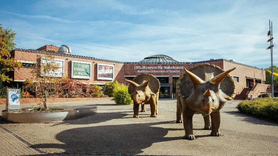 Aussenansicht des Museums mit 2 Dinosaurierfiguren und dem Namen des Museums auf Hauswand