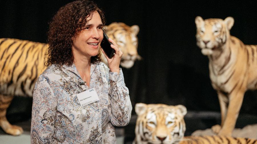 Eine redende Frau mit Telefon am Ohr vor Tigern stehend