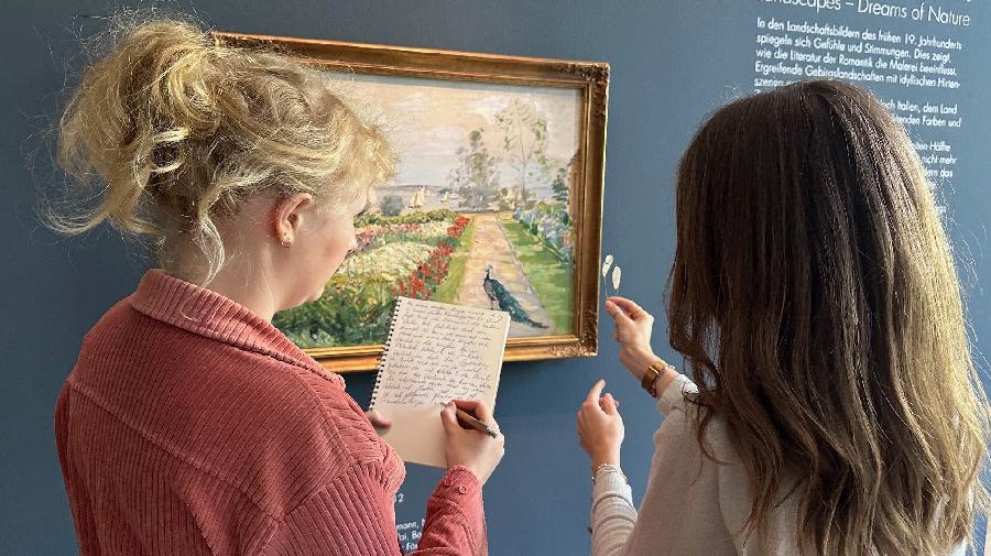 Eine Person hält einen Gegenstand hoch, und eine zweite Person schreibt in einen Block.