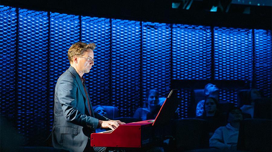 	Pianist Marcus Sukiennik steht an einem Piano unter der mit Sternen erleuchteten Planetariumskuppel