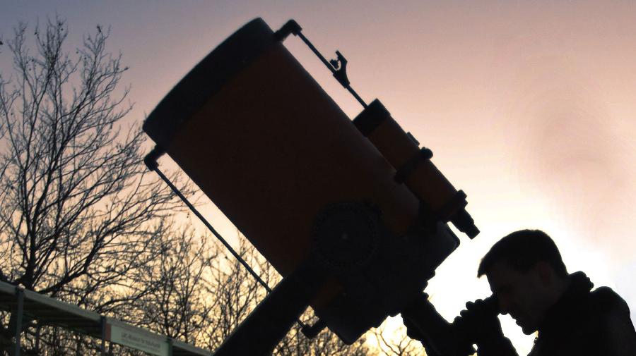 Ein Mann schaut am Abend durch ein dickes Teleskop an den Abendhimmel.