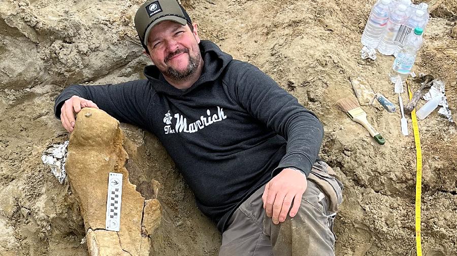 Nils Knötschke neben einem großen versteinerten Knochen liegend.