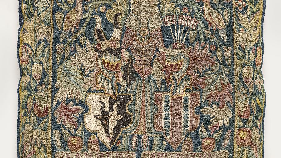 Ein Wappenkissen. Kissen mit Motiven, darunter Blätter, eine Dame und zwei Wappen mit Ritterhelmen.