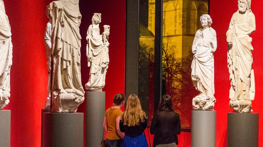 Drei Frauen stehen in der Spitze im Museum und blicken auf den Dom. Sie sind umgeben von Statuen.
