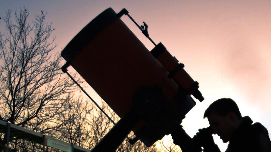 Silhouette einer Person, die bei Sonnenuntergang durch ein großes Teleskop in den Himmel schaut.