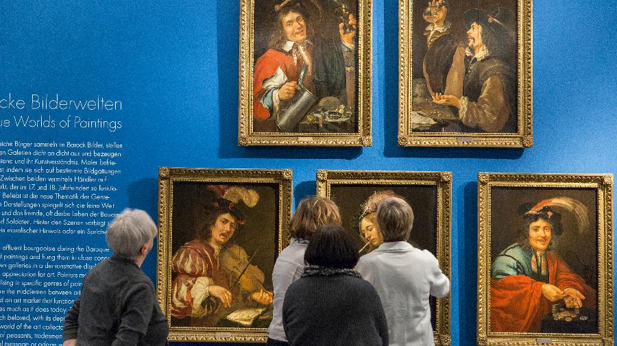 Mehrere Personen betrachten verschiedene Gemälde an der Wand.