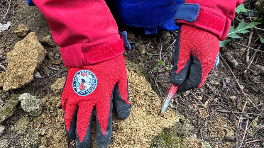 Eine Person in roter Arbeitshose mit roten Handschuhen bearbeitet mit Werkzeug einen Gesteinsbrocken
