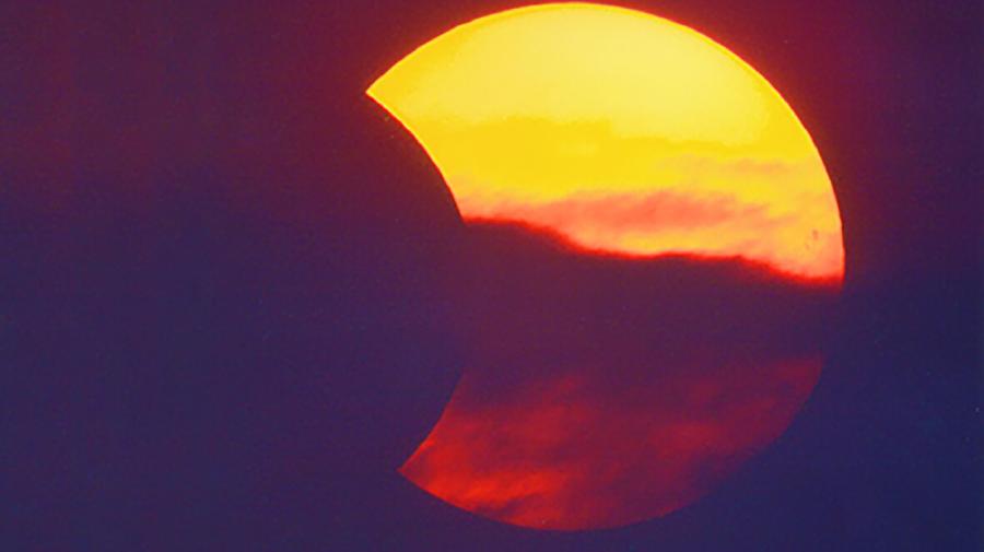 Partielle Sonnenfinsternis vor dunklem Himmel, teilweise von Wolken verdeckt.