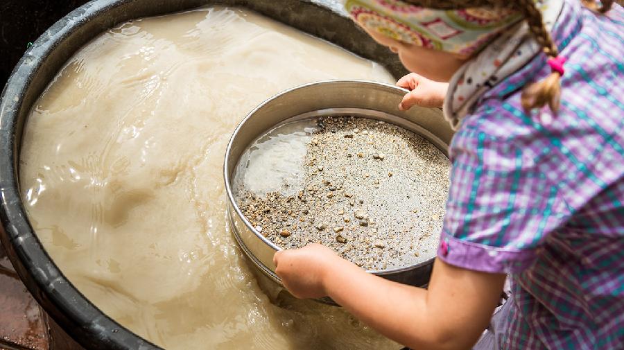 Ein Mädchen schöpft mit einer Siebschale Sand und Wasser aus einem Becken.