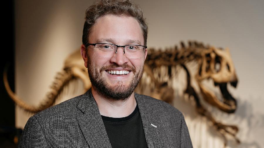 Portrait von lachendem Mann vor einem Dinosaurierskelett. 