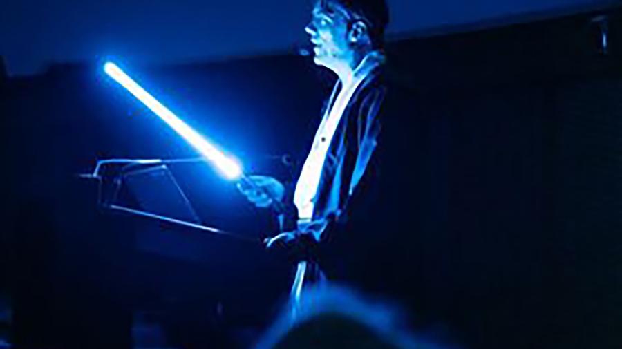 Ein Mann im dunklen Planetarium und hält ein leuchtendes Laserschwert in der Hand.
