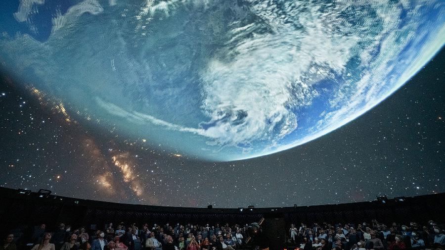 Planetariumsraum mit Stühlen. An der Kuppel ist der Ausschnitt einer Weltkugel zu sehen.