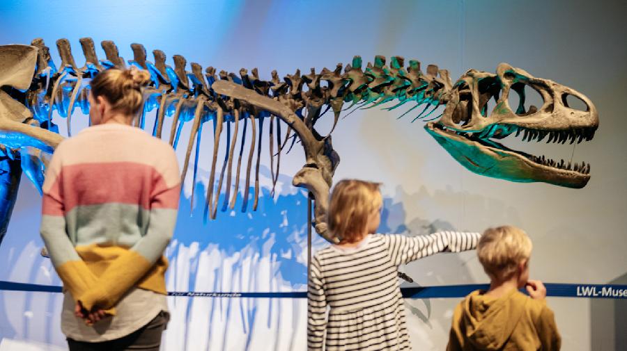 Eine Frau und zwei Kinder stehen vor einem Dinosaurierskelett.