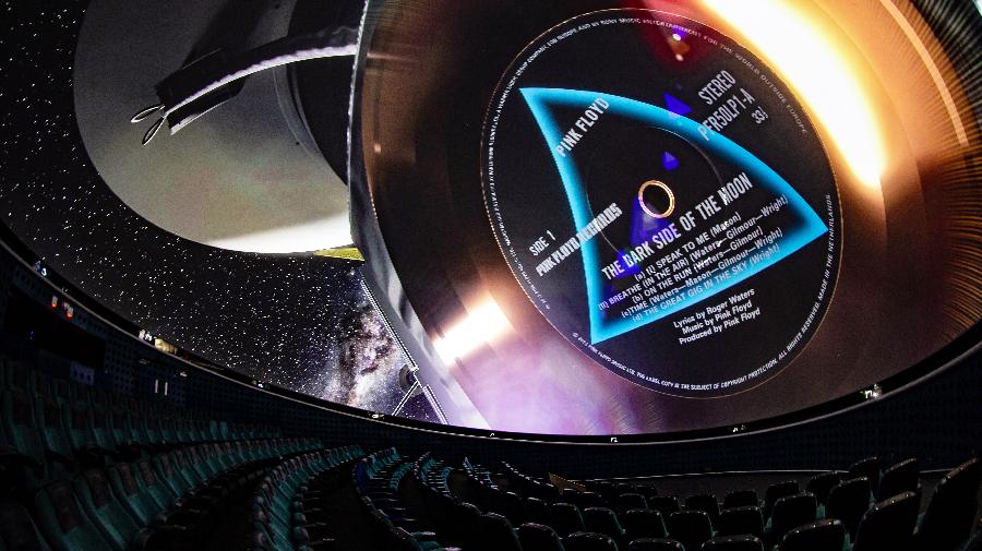Planetariumsraum mit Stühlen. An der Kuppel ist Saturn mit einer schwebenden Schalplatte zu sehen.