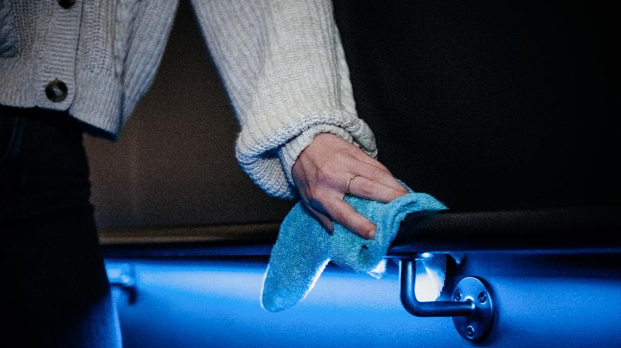 Eine Person wischt mit einem Putztuch über das Geländer im blau beleuchteten Planetarium.