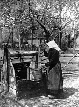 Bäuerin mit Haube beim Wasserschöpfen am Brunnen