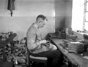Holzschuhmanufaktur: Arbeiter beim Aufbringen von Lederbeschlägen auf den Holzschuh