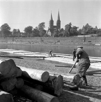 Holzflößerei auf der Weser: Flößer beim Einholen der Baumstämme - im Hintergrund die Türme der Kiliani-Kirche