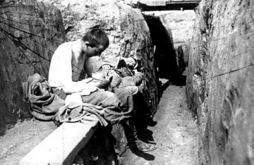 Kriegsschauplatz Vogesen/Elsass 1915: Deutscher Soldat im Schützengraben entlaust seine Kleidung