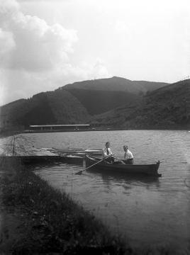 Zwei Ruderer auf einem Fischteich, im Hintergrund das Freibad in Bilstein
